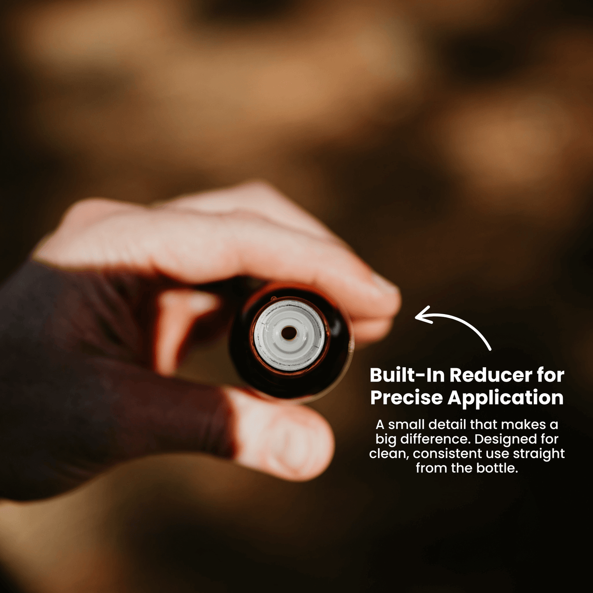 Hand holding a bottle with a built-in reducer for precise application, against a blurred background.