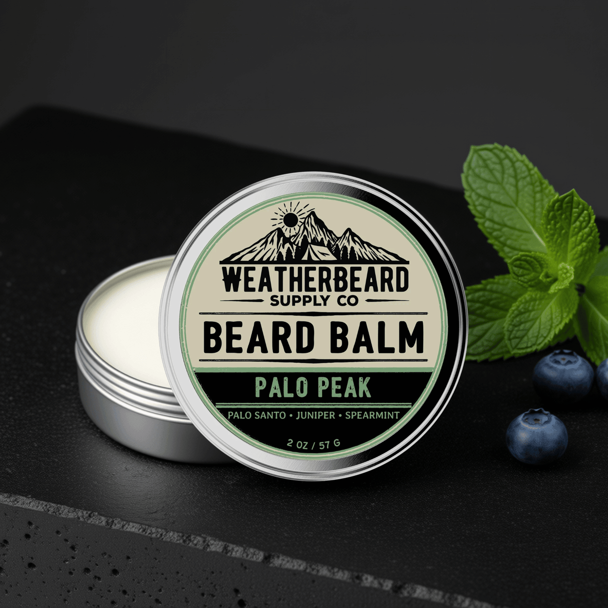 Palo Peak Beard Balm on a dark background with spearmint mint leaves and juniper berries surrounding it.
