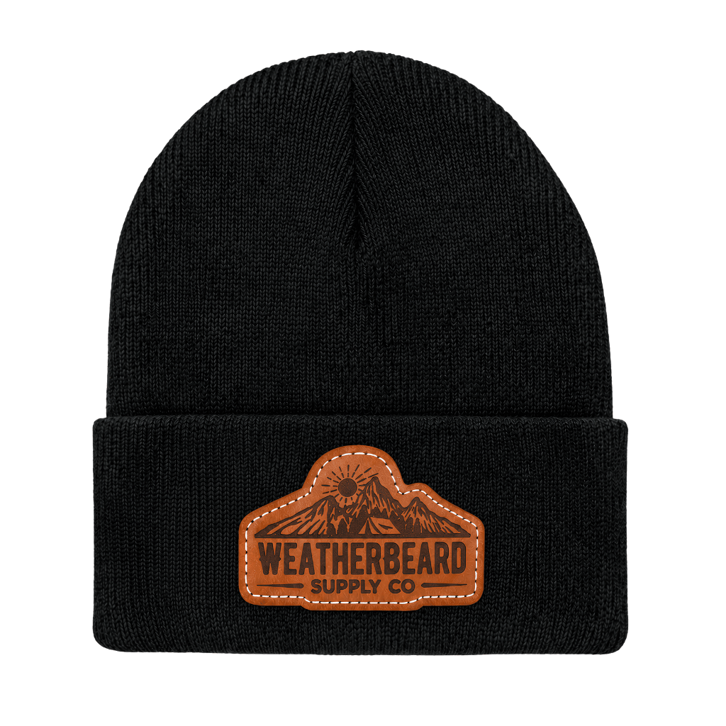 A black knit beanie hat with a brown leather patch on the front cuff that reads 'WEATHERBEARD SUPPLY CO' with a mountain graphic, shown on a plain white background.