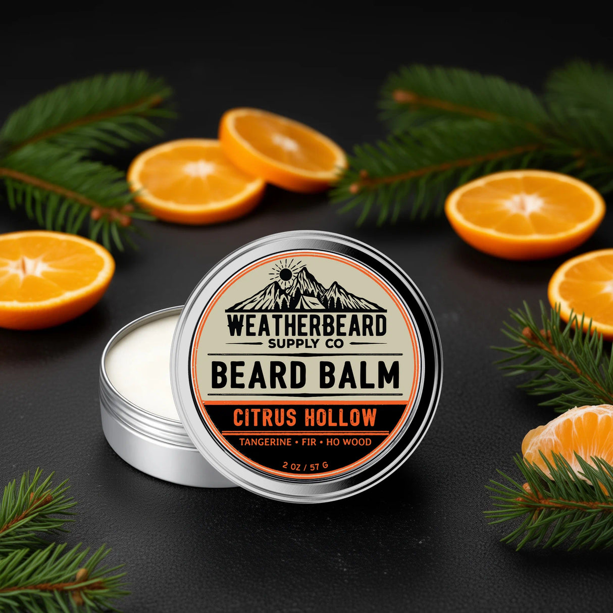 Weatherbeard Supply Co Citrus Hollow Beard Balm Tin sitting on a a black table with tangerine slices and fir needle around it