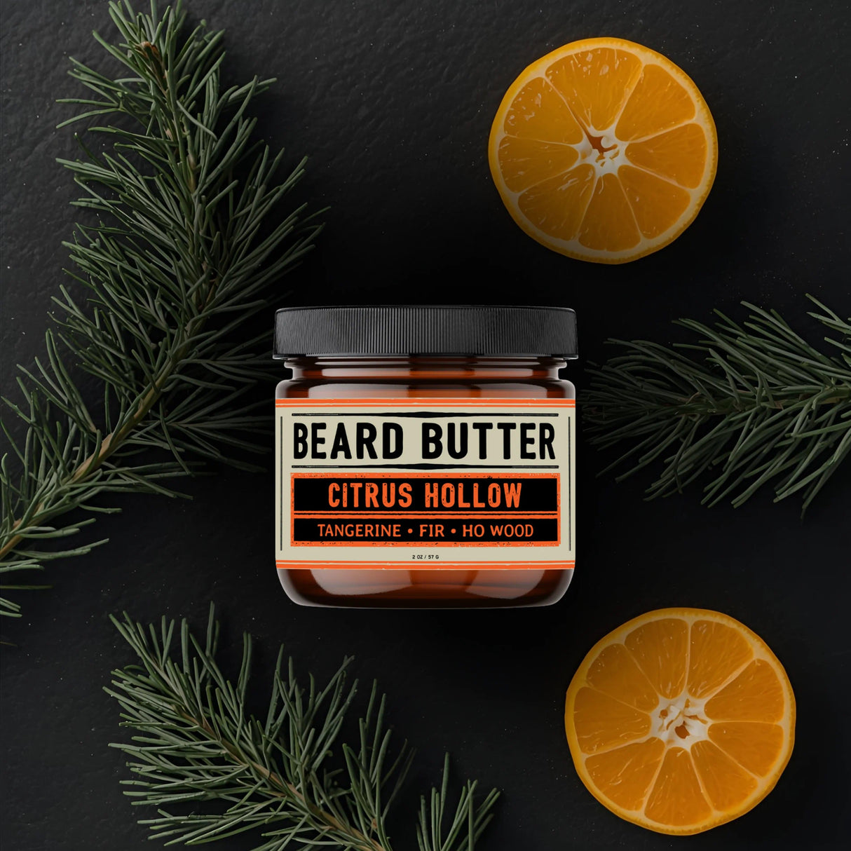 Jar of Citrus Hollow Beard Butter with tangerine slices and fir needle branches on a dark background