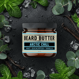 Jar of Arctic Chill Beard Butter surrounded by peppermint leaves and ice on a dark background