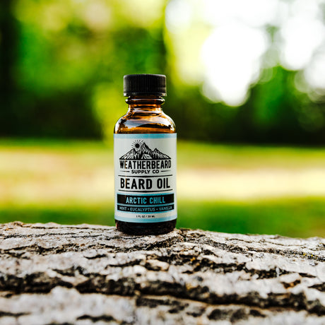 Arctic Chill Beard Oil by Weatherbeard Supply Co sitting outside on a wooden log