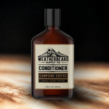 Bottle of Weatherbeard Supply Co Campside Coffee beard conditioner on a wood table in studio setting