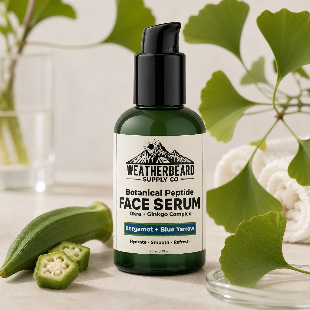 A bottle of Weatherbeard Supply Co. Botanical Peptide Face Serum in a dark green bottle with a black cap, styled with botanical ingredients including bergamot, blue yarrow, ginkgo leaves, and okra on a light marble surface.