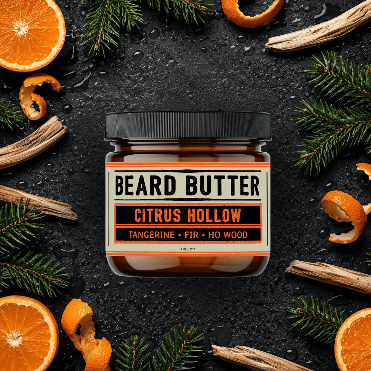 Jar of  'Citrus Hollow' Beard Butter surrounded by tangerine slices, fir needle, and wood chips on a dark background