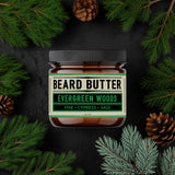 Jar of beard butter labeled 'Evergreen Woods' surrounded by pine branches and pine cones on a dark background
