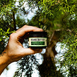 Hand holding a jar of 'Evergreen Woods' beard butter against a natural background with greenery.
