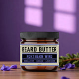 Jar of beard butter labeled 'Northern Wind' with lavender flowers on a wooden surface and purple background