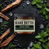 Jar of 'Beard Butter Palo Peak' surrounded by natural ingredients on a dark background