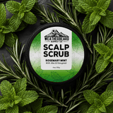 A round black tub of Weatherbeard Supply Co Scalp Scrub, Rosemary Mint, surrounded by fresh green rosemary and mint leaves on a dark slate background.