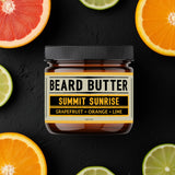 Jar of 'Summit Sunrise' beard butter surrounded by sliced citrus fruits on a black background