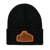 A black knit beanie hat with a brown leather patch on the front cuff that reads 'WEATHERBEARD SUPPLY CO' with a mountain graphic, shown on a plain white background.