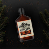 Bottle of Weatherbeard Supply Co. beard wash with a dark background and fir needles surrounding it