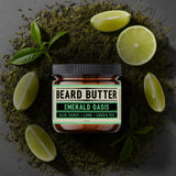 Jar of beard butter labeled 'Emerald Oasis' surrounded by green tea leaves and lime slices on a dark background