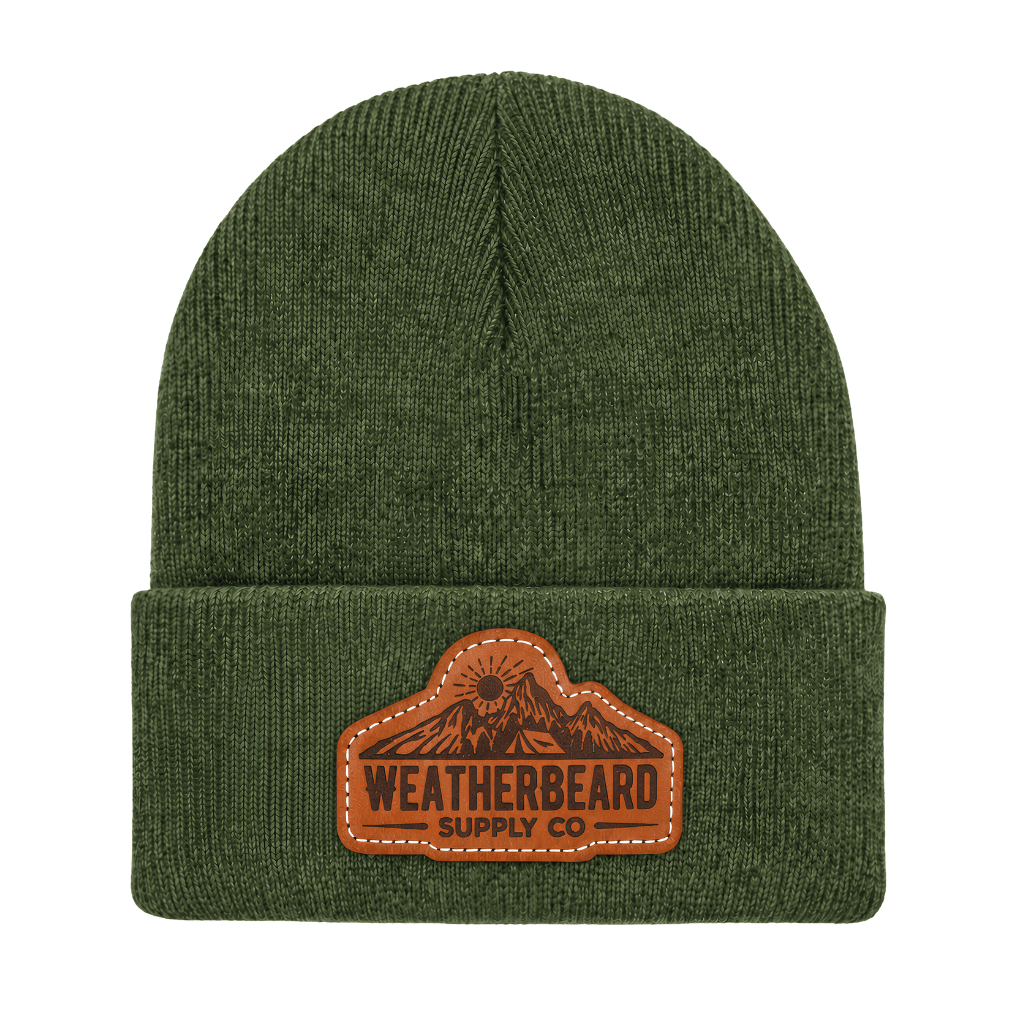 An olive green ribbed knit beanie hat with a brown leather patch on the front cuff that reads 'WEATHERBEARD SUPPLY CO' with a mountain graphic.