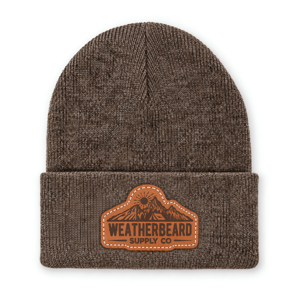 A brown ribbed knit beanie hat with a folded cuff, featuring a brown leather patch on the front that reads 'WEATHERBEARD SUPPLY CO' with a mountain graphic, shown on a plain white background.