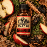 A bottle of Weatherbeard Supply Co. Beard Oil in Orchard Valley, styled in a flat lay with apple slices, wood bark, pine needles, and dried fruit on a forest floor background.