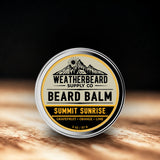 Tin of Weatherbeard Supply Co. Beard Balm Summit Sunrise on a wooden surface with a dark background