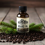 Bottle of Weatherbeard Supply Co. Campside Coffee beard oil with coffee beans and spruce branches on a wooden table