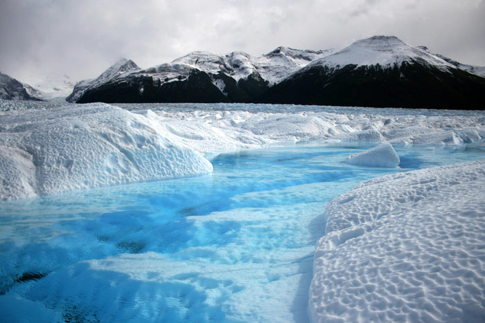 Glacier with blue water and snow-covered mountains in the background