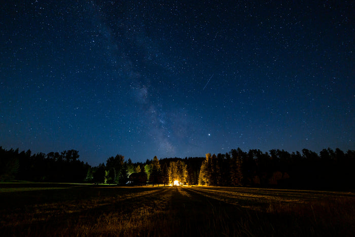Starry night sky over a field with a light source in the distance